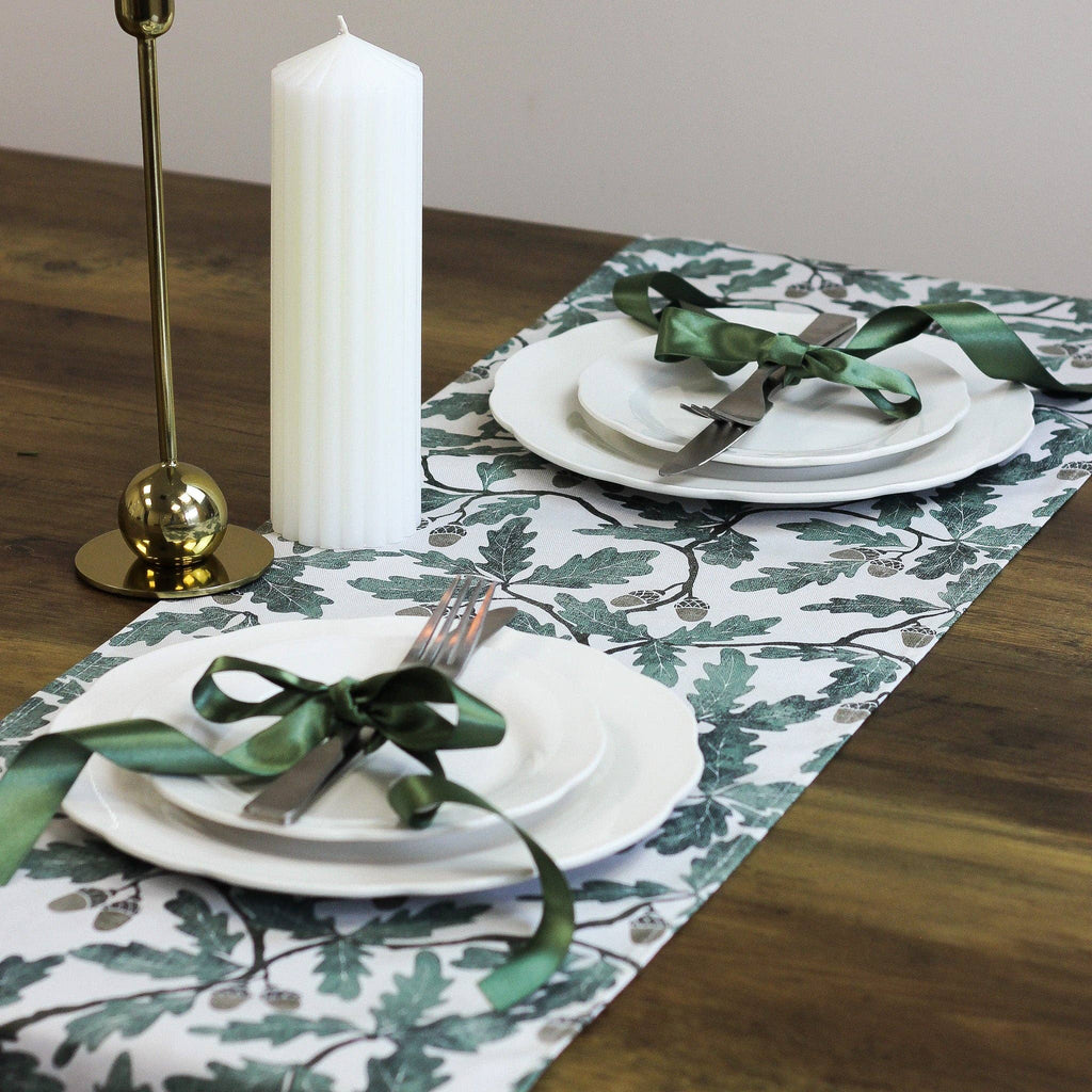Table setting with white plates, green ribbons, and a candle on a decorative table runner.