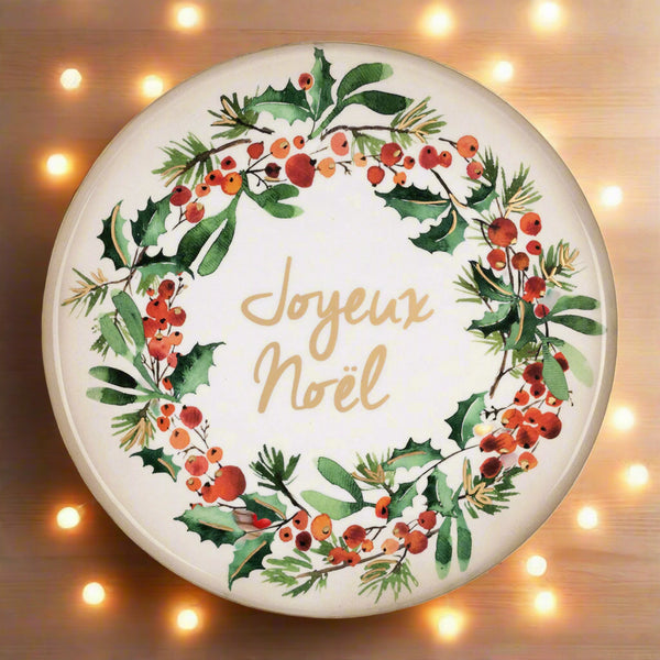 Round ceramic plate with Christmas wreath design and 'Joyeux Noel' text on a white background