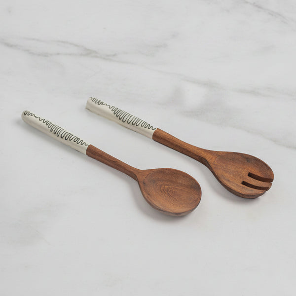 Two wooden serving utensils, a spoon and a salad spinner, with white handles featuring a black textured pattern, displayed on a light gray background.