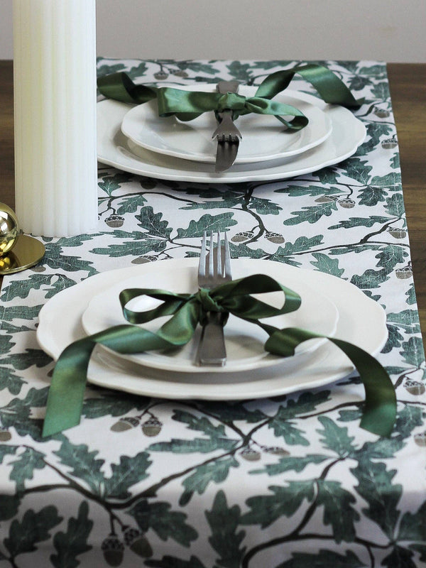 Set table with white plates, silverware, and green ribbons on a patterned tablecloth.