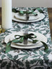 Set table with white plates, silverware, and green ribbons on a patterned tablecloth.