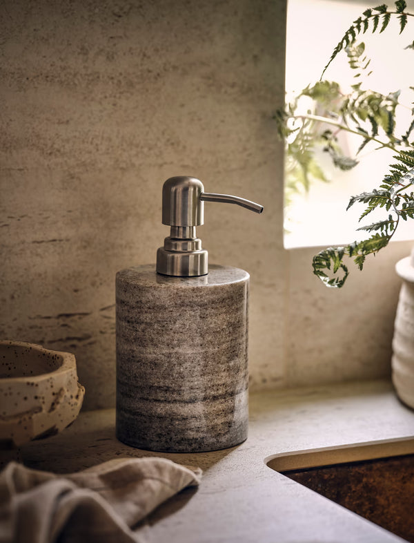 Soap dispenser on a kitchen counter with a plant in the background