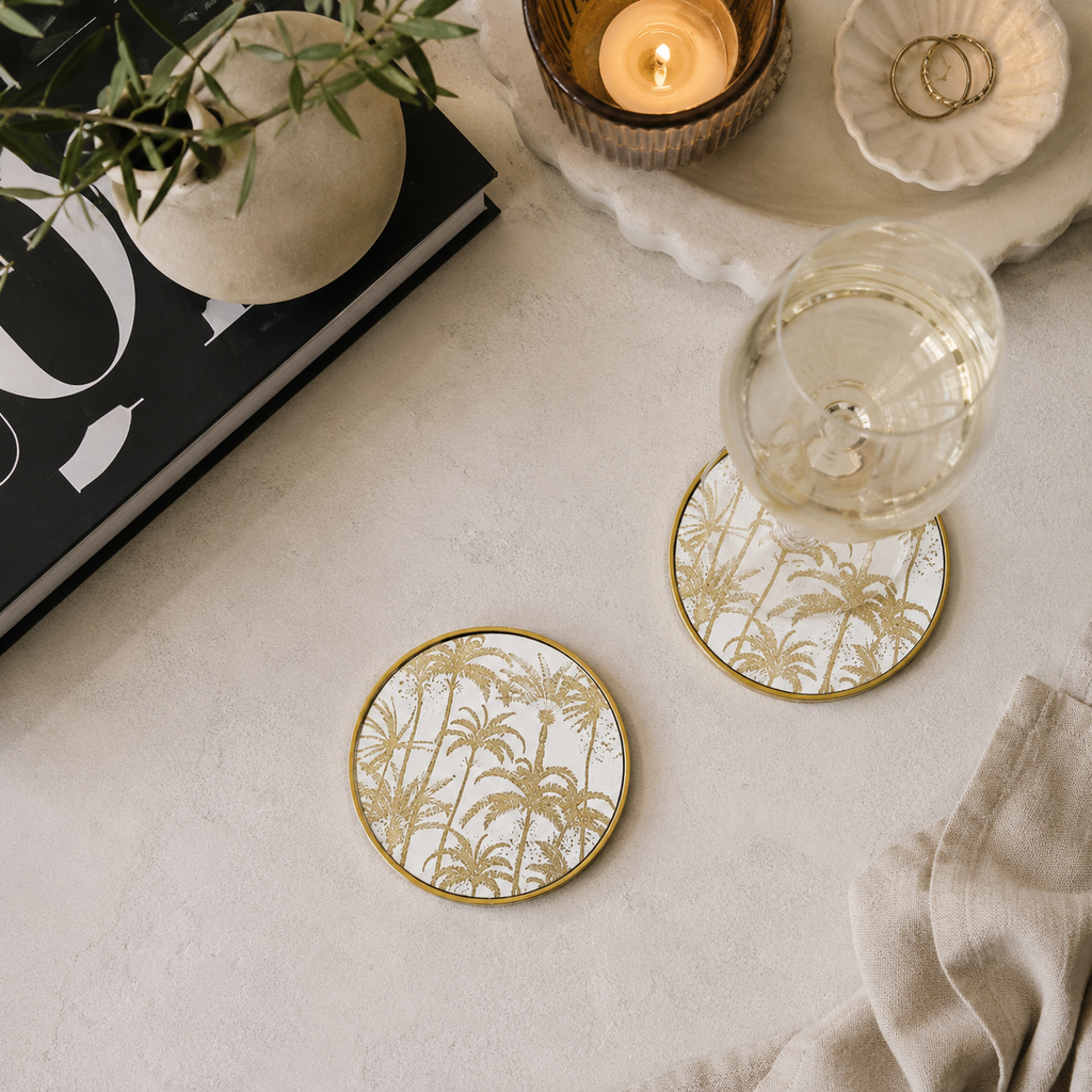 Coasters with palm tree design on a table with a glass of wine, candle, and book.