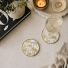 Coasters with palm tree design on a table with a glass of wine, candle, and book.