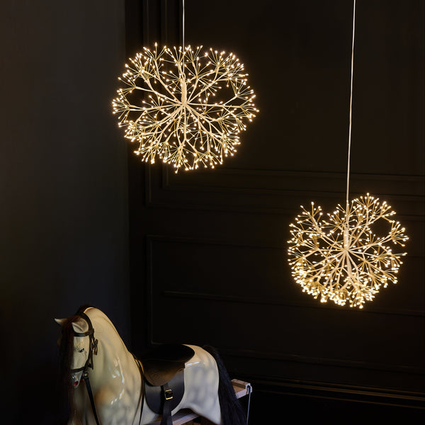 Two spherical string lights hanging above a rocking horse on a wooden floor with a dark wall background.