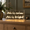 All Is Calm All Is Bright Neon Sign on an oak sideboard with Christmas greenery
