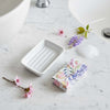 Orange blossom soap in floral wrapping beside a white ceramic soap dish