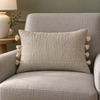 Taormina natural linen cushion with four stitched rows and eight tassels on a grey armchair